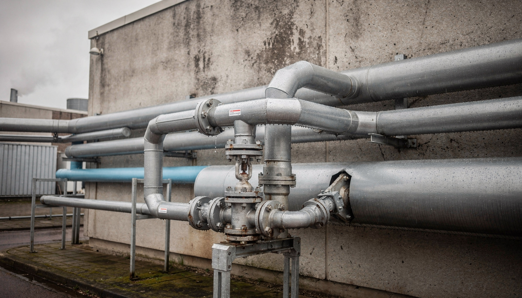 Industriële koelbuizen en een metalen waterklep bij een datacenter, met condens en lichte stoom.