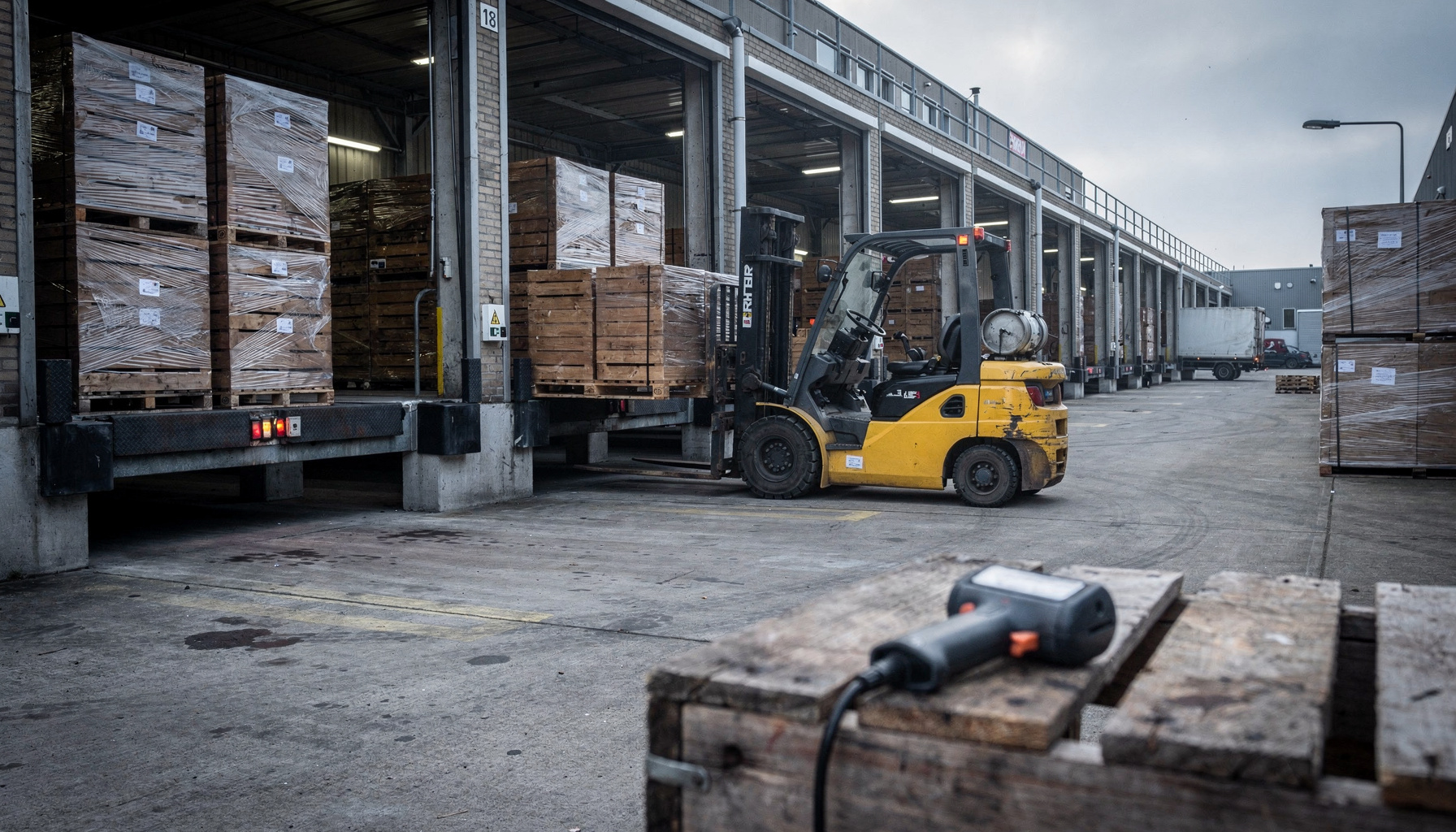 Pallets en een forklift staan klaar op het laadperron van een transportbedrijf in het vroege ochtendlicht.