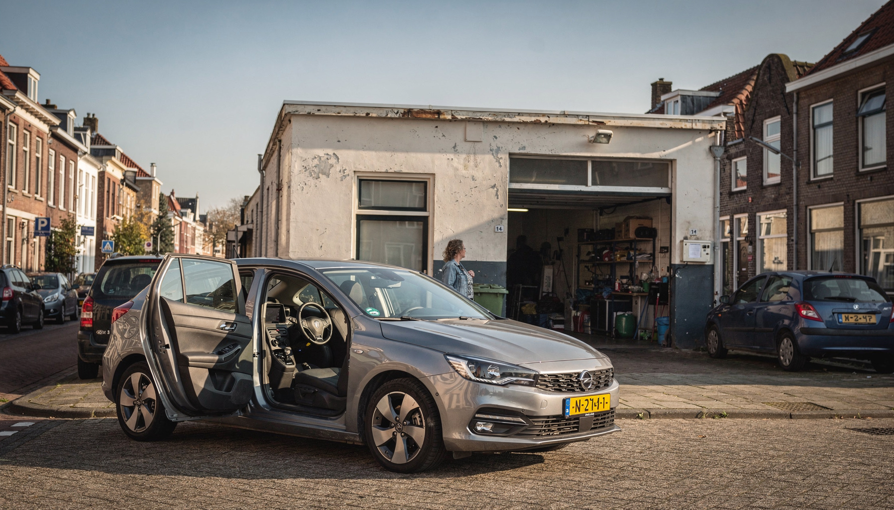 Een betaalbare hatchback staat voor een autowerkplaats, terwijl een vrouw in de verte naar binnen loopt voor onderhoud