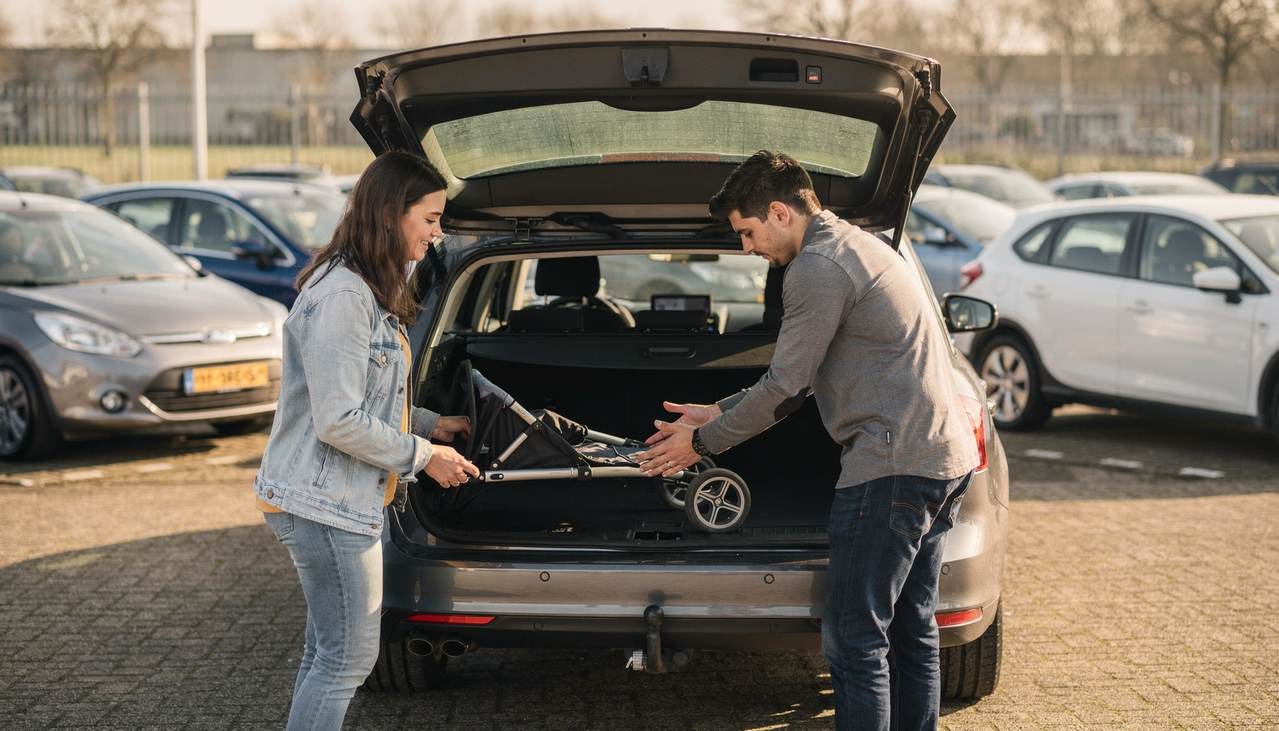 Een koppel test of een kinderwagen in de kofferbak van een stationwagon past, naast een hatchback en een MPV.